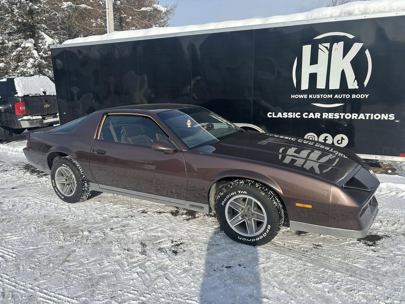 Copper-brown Camaro beside the Howe Kustom trailer in winter